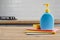Yellow sponge and blue plastic bottle on wooden table with color cloths, kitchen background