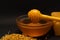 A yellow spoon of honey dipped in a jar of honey and bee bread scattered on a black background. Honey dripping around
