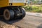 Yellow steamroller or soil compactor working on asphalt road at construction site