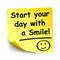 Yellow sticker with black postit â€žStart your day with a smile!!!â€œ, note hand written - vector