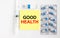 Yellow sticker with text Good Health on a white background with syringes, pills and ampoule