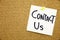 A yellow sticky note writing, caption, inscription Phrase CONTACT US in black ext on a sticky note pinned to a cork