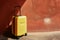 A yellow suitcase rests against a red wall, creating a striking contrast