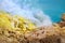 Yellow sulfuric rocks, poisonous smoke and a sulphurous blue lake of crater Ijen Volcano. Caldera of an active volcano.