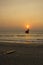 Yellow surfboard lies on the sand near the red flag against the ocean during sunset