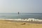 Yellow surfboard lies on a sandy beach near a red flag against a blue ocean with waves and a clear sky