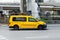 Yellow Taxi minivan driving on a city road in the background of an industrial area