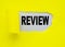 Yellow torn paper with a hole and the word REVIEW on a gray background, the concept OF ANALYSIS AND VERIFICATION