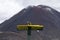 Yellow tourist guidepost sign on the great walk Tongariro Alpine Crossing. In the background active volcano Mt Doom, Mt Nguarahue.