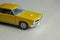 Yellow toy car on gray striped surface. Model of classic muscle car with shadows and partly soft focus. Perspective view of auto