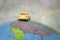 A yellow toy car is traveling around the globe. Back view The car is located on the American continent of the world map. The conce