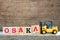 Yellow toy forklift hold letter block A to complete word Osaka