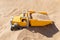 Yellow toy truck buried among the sand lit by sunlight.