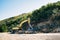 Yellow tracked tractor drills stones near the mountain. Wide angle