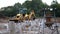 A yellow tractor bulldozer excavator digs a trench with a bucket between reinforced concrete piles.