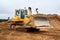 A yellow tractor bulldozer stands in a sand pit