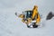 Yellow tractor excavator with large bucket clears snowy road from snow