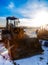 Yellow tractor on golden sunrise sky winter