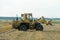 A yellow tractor with the help of a manipulator puts round bales of hay on a trailer. Transportation of hay bales in meta storage