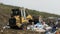 Yellow tractor works on dump. Household garbage. Waste sorting on landfill of big city. Preparation for recycling.