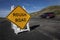 Yellow traffic control sign stating Rough Road on highway shot in late afternoon sun. A car is visible blurred driving past.