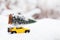 Yellow truck hauling a Christmas tree home through a snowy winter forest