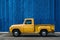 Yellow truck parked in front of blue wall, copy space