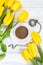 Yellow tulips, a cup of coffee, cappuccino and vintage watch on a chain on a white wooden