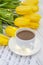 Yellow tulips with garlands, a cup of coffee, cappuccino and notes on a white wooden