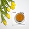 Yellow tulips with notebook with a tea on a white background