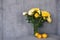 Yellow tulips, roses, chrysanthemums in a transparent vase against the background of a gray concrete wall. A bouquet of fresh spri