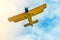 Yellow two-pilot airplane in the blue cloudy sky