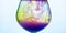 Yellow and violet paints fall in a wineglass with water