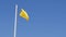 Yellow warning flag on the mast waving in the wind on the beach against the blue sunny sky