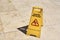 Yellow wet floor caution sign in summer day, closeup