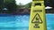 Yellow wet floor caution sign on swimming pool background in amusement water park. Caution wet floor sign in aqua park