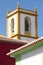 Yellow and white bell tower with colorful buildings.