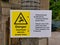 A yellow and white danger sign on the Leeds to Liverpool Canal in Lancashire, UK warning anglers of overhead electric power lines