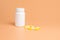 Yellow and white pills, tablets and white bottle on orange background