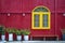 Yellow window, flowerpots with plants and bench on the background of a red metal wall on the street of Danang city in Vietnam