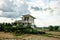 Yellow wooden house, decorated with plants and flowers, stands in the middle of farmland, mountain, and blue sky