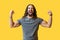 Yes! Portrait of happy rejoicing bearded young man with long curly hair in grey tshirt standing, raised arms and celebrating his