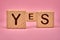 YES word on wooden cubes. Yes message made with building blocks. Copy spaceYES lettering on pink background. Pink