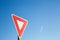 Yield sign against a blue sky with a contrail.