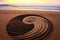 yin yang symbol drawn on a sandy beach at sunset