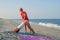 Yoga class instructor helps beginner to make asana exercises. Woman doing downward facing dog exercise with trainer on the beach