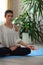 Yoga at home. Keep calm. Attractive young woman sitting on lotus position on floor with eyes closed on blue mat in white shirt