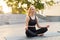 Yoga and Meditation in Modern City Caucasian Woman Relax Lotus Position Sitting Yoga Mat Outdoors Summer Park on Concrete floor