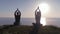 Yoga outdoor during sunset, athletic pair meditating in lotus position on top of mountain and looking at the sea, view