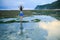 Yoga pose. Woman standing on the rock, practicing yoga. Young woman raising arms with namaste mudra at the beach. View from back.